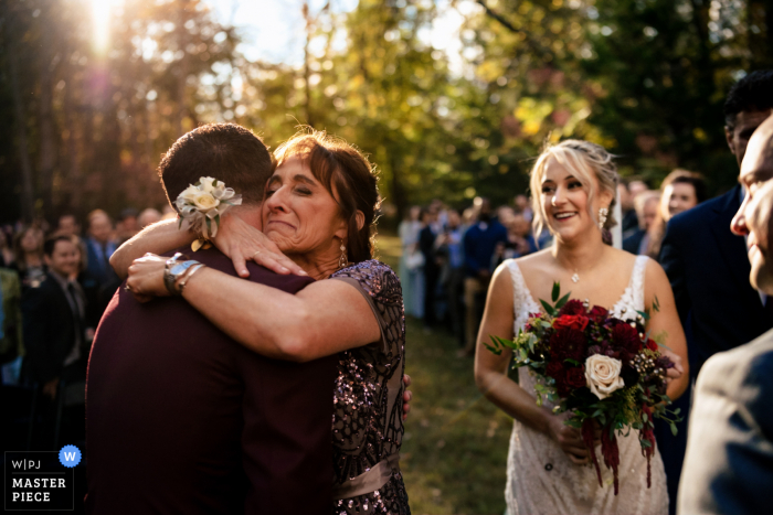 Um fotojornalista de casamento capturou este momento em Prince William Forest em Washington DC mostrando A mãe da noiva abraça seu novo genro enquanto ela o ajuda a dar a noiva