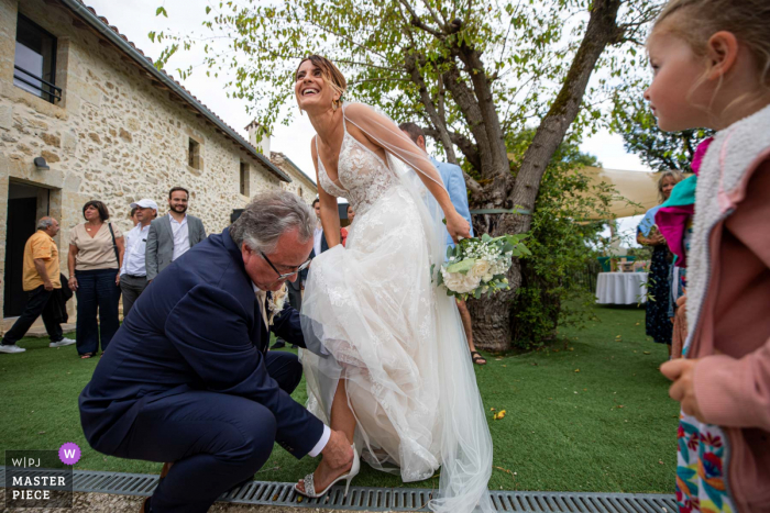 Um fotógrafo de reportagem de casamento da França capturou este momento mostrando a noiva apertando o calcanhar durante uma festa no jardim e seu pai a ajuda