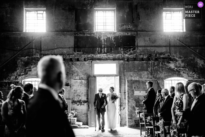 A top wedding reportage photographer captured this picture at the Asylum Church in London as the Bride enters the chapel with her father the chapel was bombed in WWII