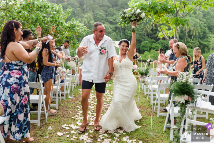 Dokumentalny fotograf ślubny uchwycił to zdjęcie w Jaco Beach, Puntarenas, Kostaryka, przedstawiające pannę młodą i pana młodego opuszczających ceremonię podczas świętowania w nieoczekiwanym deszczu