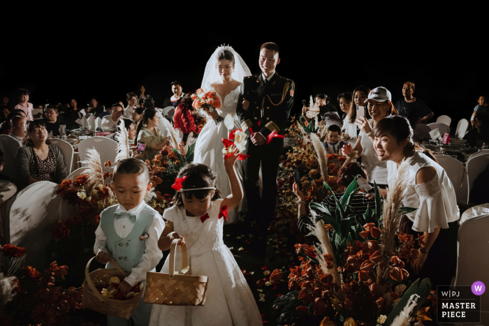 Um importante fotógrafo de documentários de casamento de Sichuan criou esta imagem mostrando Os recém-casados ​​subiram ao palco e a garotinha jogou as pétalas para o céu. Família e amigos os assistiram