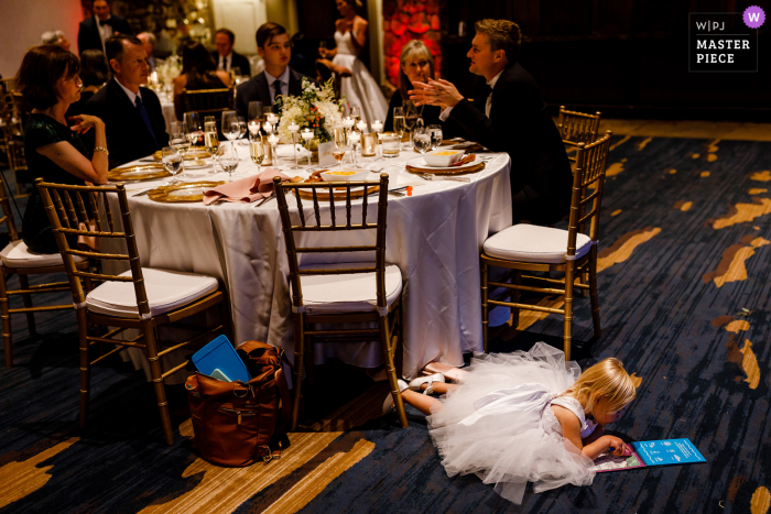 A top wedding photojournalist from Colorado created this image a the Reception of a Flower girl taking a break by the venue tables