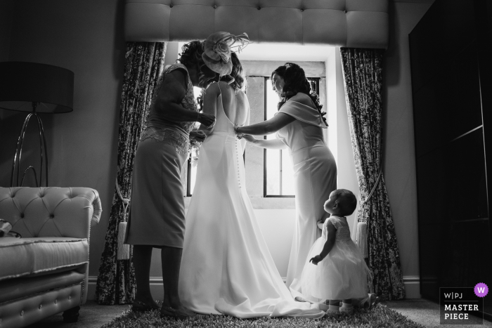 A documentary wedding photographer at the Merrydale Manor captured this picture of the Bride getting in her dress and flower girl looking on