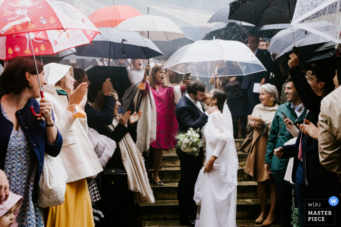 Ein Hochzeits-Fotojournalist in Chaumont in Vexin hat diesen Moment während eines Kirchenaustritts für das Paar unter Regenschirmen festgehalten Ein Hochzeits-Fotojournalist in Chaumont in Vexin hat diesen Moment während eines Kirchenaustritts für das Paar unter Regenschirmen festgehalten