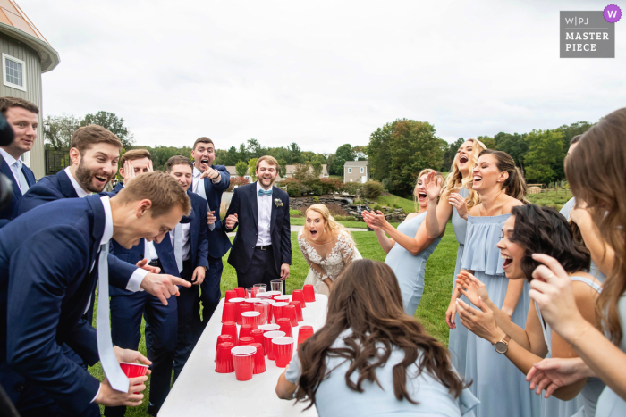 View this fine example of the best in the world wedding photography at the Bear Brook Valley in Fredon, New Jersey showing us the Bridal party reacting during game of Flip Cup