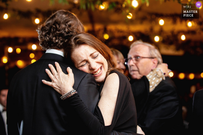 View this emotional wedding image in Montclair, New Jersey of the mother of groom smiling and hugging groom while dancing