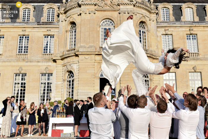 Une image de mariage de style documentaire à Lille montrant un moment à l'extérieur des meilleurs amis des mariés jetant la mariée en l'air