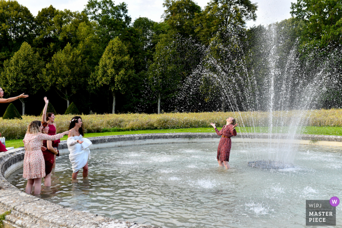 Ein französischer Dokumentarfilm-Hochzeitsfotograf hat dieses Bild der Braut und ihrer besten Freunde aufgenommen, die während der Cocktailstunde in einem Wasserbrunnen zusammen spielen