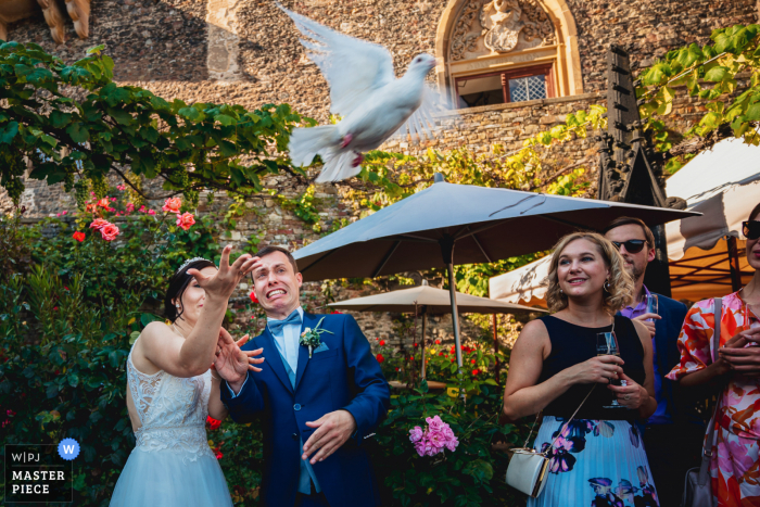 A top wedding photojournalist at the Rheinstein Castle created this image of a dove taking flight outdoors by the bride and groom