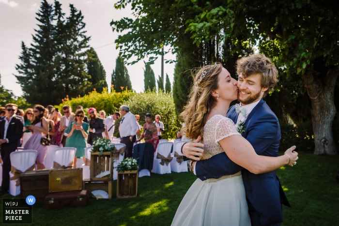 Um documentário fotógrafo de casamento do Domaine de la Baraque de Sèrignac tirou esta foto de um abraço e um beijo para a noiva e o noivo na cerimônia de casamento ao ar livre