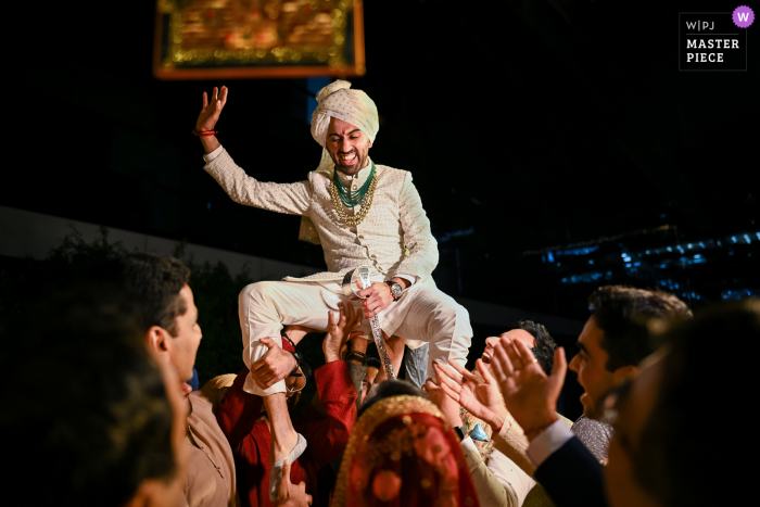 A Pune documentary wedding photographer in India captured this moment showing grooms friends lift him high up so that the bride cannot reach him for the garland exchange all in good fun of course