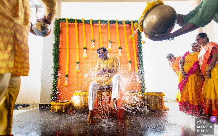 Een huwelijksfoto in de stijl van een Indiase documentaire die een moment toont tijdens een evenement van de bruidegomdouche, een traditioneel ritueel in een Zuid-Indiase bruiloft waarbij de bruidegom of de bruid worden bespat met water tijdens hun pre-huwelijksritueel