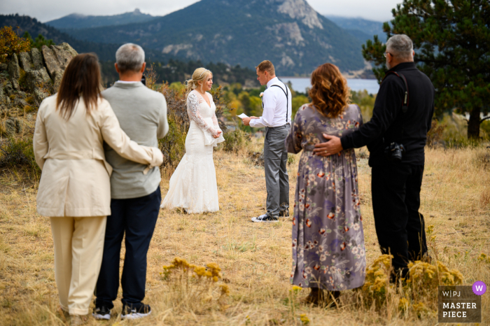 Bekijk deze trouwfoto van dit cruciale moment in het Rocky Mountain National Park van de ouders van de bruid en bruidegom die kijken hoe hun kinderen weglopen tijdens een gelofteuitwisseling in de buitenlucht