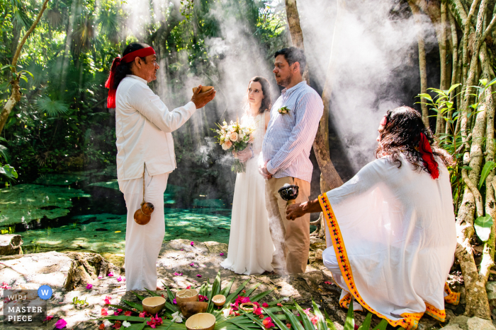 Uma imagem de casamento no estilo documentário do México mostrando um momento no Cenote Cristalino Puerto Aventura Riviera Maya durante uma cerimônia de casamento maia no cenote