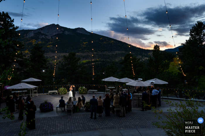 Um fotógrafo de casamento documental do Colorado em Estes Park capturou esta foto da noiva e do noivo durante sua primeira dança, enquanto seus convidados olham ao ar livre ao anoitecer