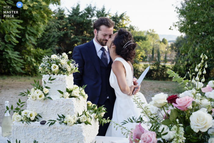 Un grand photographe de mariage documentaire d'Arezzo à la Villa Santa Maria a créé cette image du baiser et du couteau avec le gâteau à l'extérieur