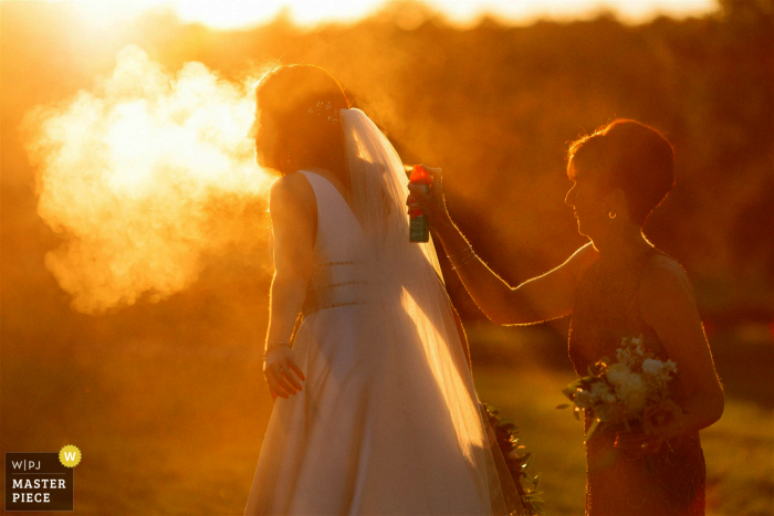 View this dramatic Yarmouth, MA wedding image of a backlit application of bug spray on the bride outdoors