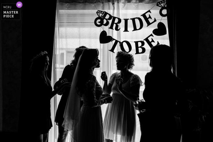 Constanta, una fotoperiodista de bodas en Mamaia, capturó este momento en BW of the Bride preparándose cerca de una ventana debajo de un letrero que decía Bride To Be