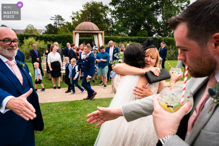 Un fotógrafo de bodas documental de Worcestershire capturó este momento en The Wood Norton mostrando Un abrazo entre la novia y su madre y un apretón de manos del padre de la novia para el novio.