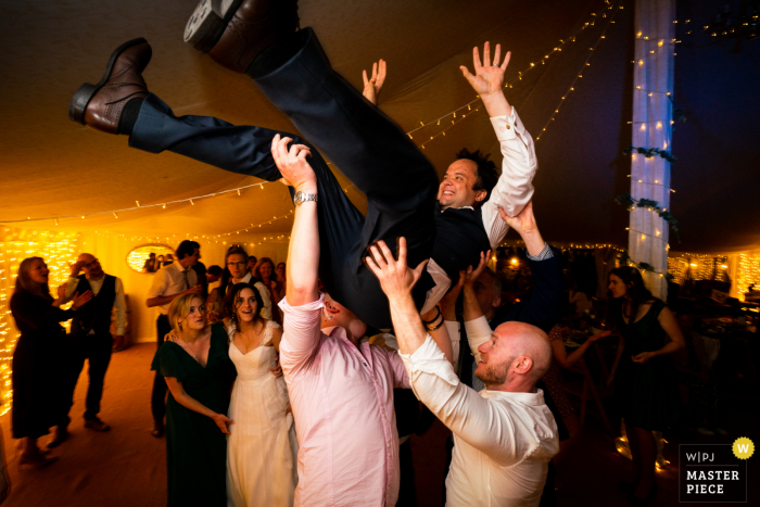  An Oxford wedding reportage photographer captured this moment at The Perch of The groom lifted up by his friends at the end of the night