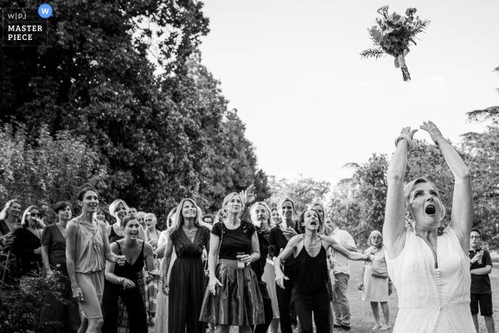 Un destacado fotoperiodista de bodas de Ramonville en Domaine de Montjoie creó esta imagen de BW durante el lanzamiento del ramo al aire libre