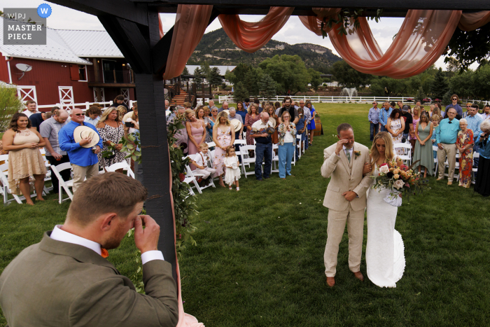 A top Colorado wedding photojournalist at the Crooked Willow Farms created this image showing the groom and father of the bride wiping tears from their eyes at the beginning of the wedding ceremony