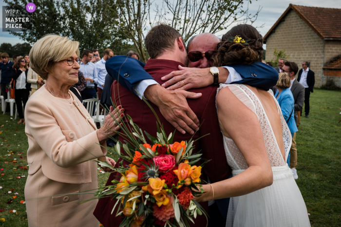 Ein dokumentarischer Hochzeitsfotograf aus Lyon in Frankreich hat dieses Bild eines emotionalen Papas aufgenommen, der das Brautpaar draußen umarmt