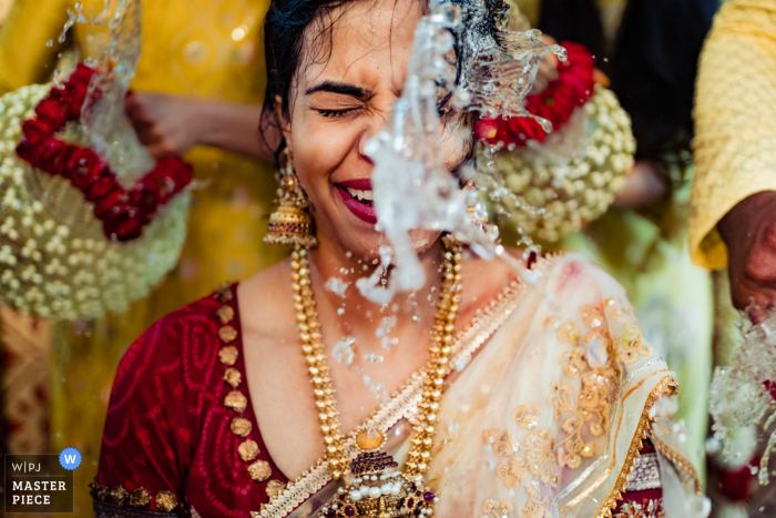 Sehen Sie sich diesen wichtigen Moment in Hyderabad Hochzeitsbild von Die Reaktion der Braut in dem Moment an, als ihre Familie und Freunde während ihrer Mangalsnanam-Zeremonie Wasser auf sie spritzen