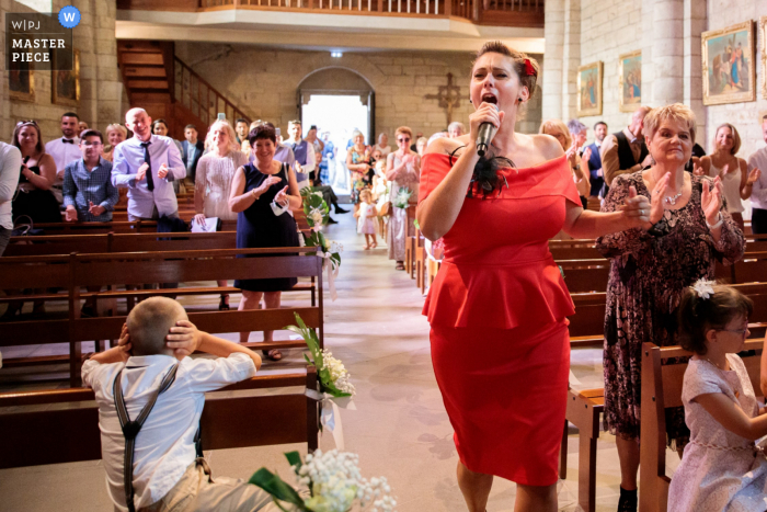 A top France wedding reportage photographer at Church of Caux captured this picture of A singer in the church, obviously too loud for this little boys taste