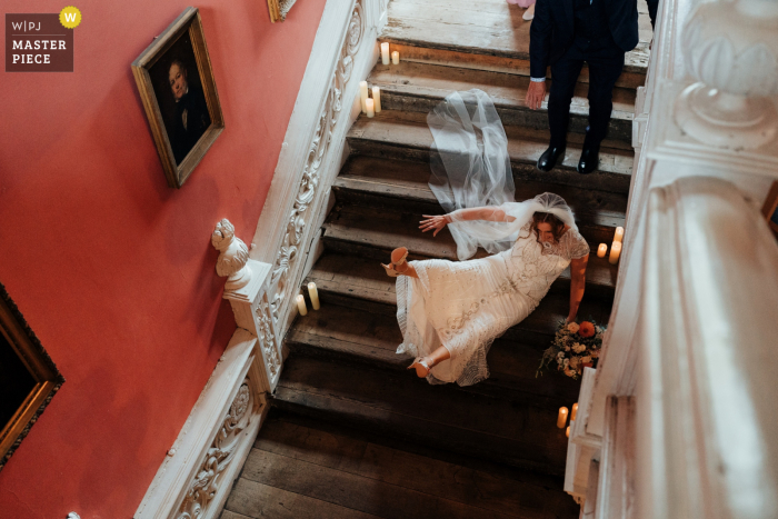 A Nottingham wedding reportage photographer captured this moment at Holme Pierrepont Hall showing the Bride falls down stairs