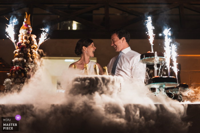 Um fotojornalista de casamento na França em Bordeaux capturou esta imagem do casal e do bolo de casamento com névoa de gelo seco e fogos de artifício.