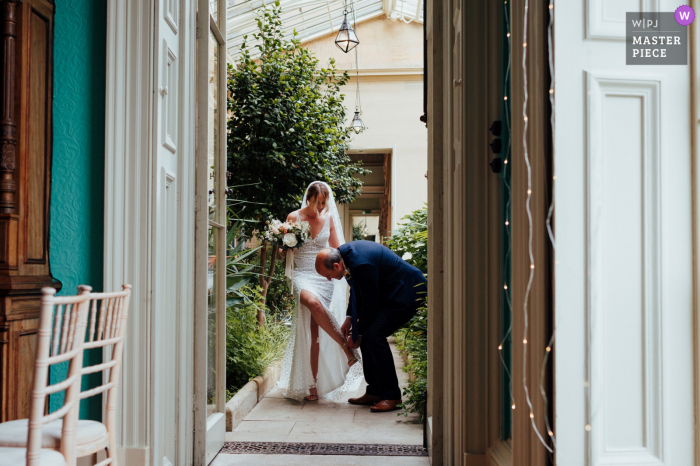 Ein Top-Fotograf für Hochzeitsreportagen aus Leicestershire in Prestwold Hall hat dieses Bild aufgenommen, das zeigt, wie der Vater der Braut den Brautschuh repariert, während er den Gang hinuntergeht