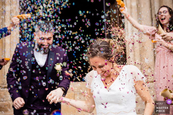 Vea este momento clave en la foto de boda de Cathédrale de Langres de la pareja saliendo de la iglesia bajo una lluvia de burbujas y confeti