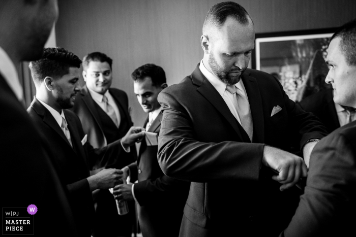 A Pennsylvania wedding reportage photographer captured this moment in BW showing the Groomsmen working together to figure out their pocket square situation