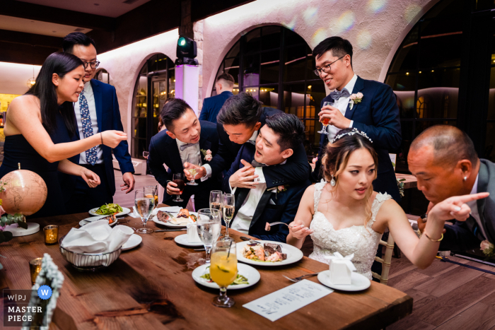 A top wedding photojournalist from Philadelphia created this image of the Bride and groom desperately trying to eat dinner while a constant parade of people interrupt them