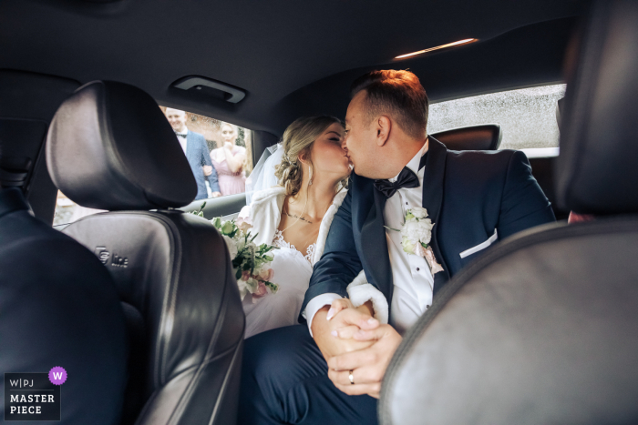 A Poland documentary wedding photographer captured this moment at the Roman Catholic Parish of the Assumption of the Blessed Virgin Mary in Czamocin of Wedding couple in the backseat of the car on their way to their wedding party