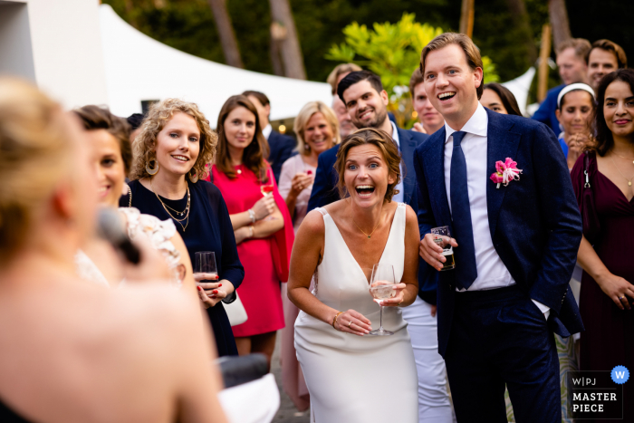 Een top trouwfotojournalist uit Utrecht in Nederland creëerde dit beeld van de bruid en bruidegom die lachen tijdens de toespraken in de buitenlucht