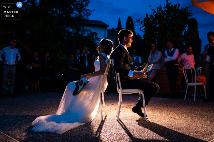 Um fotojornalista de casamento da Itália no Castelvecchio Sagrado em Gorizia registrou este momento dos jogos de casamento com a noiva e o noivo segurando sapatos