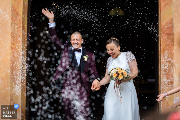 Een Italiaanse trouwfoto in documentairestijl met een moment in de San Leonardo-kerk in Verbania van de bruid en bruidegom die naar buiten gaan onder regenende confetti