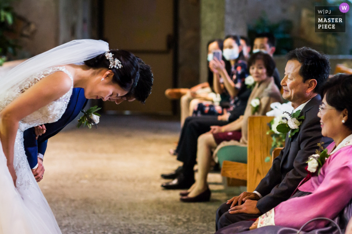 A top documentary wedding photographer from California created this image showing the Newlywed couple bowed deeply to thank their parents