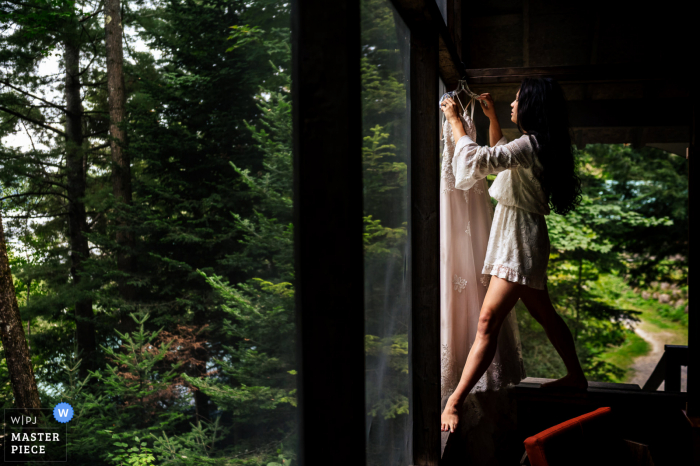 A New York documentary wedding photographer captured this moment at Timberlock Camp in Indian Lake as The bride uses her climbing skills to get her dress down