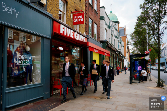 Ein Top-Fotograf für Hochzeitsreportagen in London hat dieses Bild des Bräutigams und der Trauzeugen aufgenommen, die zur Kirche gehen – es sind 5 Jungs, die an einem Five Guys-Restaurant vorbeigehen