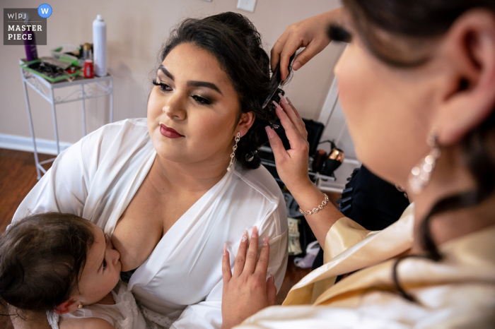 A Sevierville, TN documentary wedding photographer captured this image showing that Getting the last touches on her hair did not prevent this bride from feeding her baby