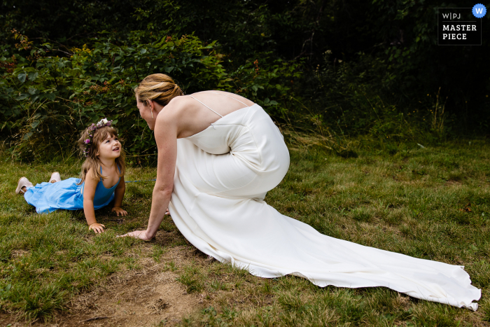 Ein dokumentarischer Hochzeitsfotograf aus Bar Harbor, Maine, hat diesen Moment festgehalten und zeigt, wie eine Braut mit einem Blumenmädchen auf dem Gras plaudert