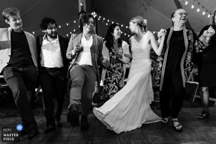 A Blue Hill, Maine documentary wedding photographer captured this moment showing The bride dancing with her friends and family