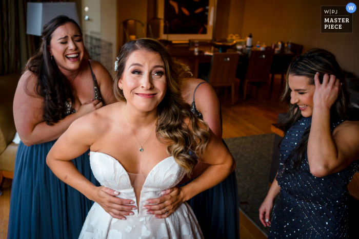 Un fotoperiodista de bodas en Georgetown DC en el Westin capturó este momento cuando las damas de honor ayudan a la novia a ponerse el vestido.