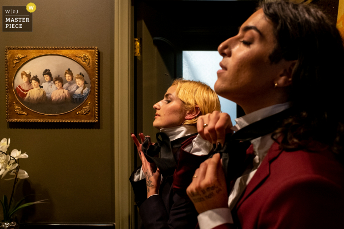 A top wedding photojournalist created this image at the Houdini Mansion in Los Angeles, California showing Two wedding party people tie their ties in the mirrors