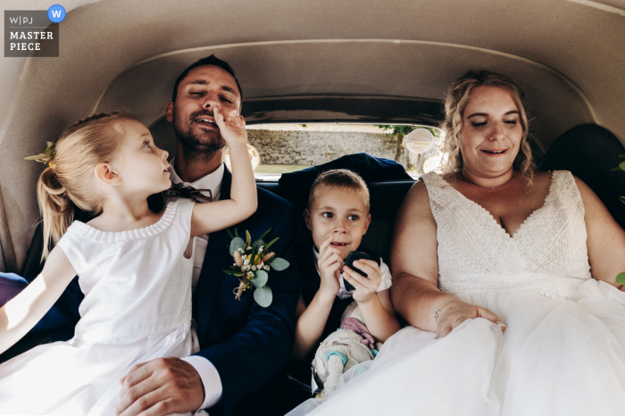 El fotoperiodista del reportaje de bodas de Oradour su Glane creó esta imagen que muestra a los recién casados ​​y sus hijos en el automóvil que los lleva al ayuntamiento mientras la hija del novio quiere sacar algo de la nariz de su papá.