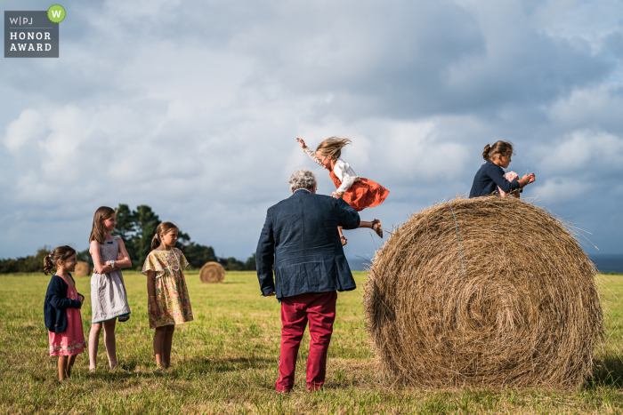 Wyjątkowe zdjęcie ślubne Belle île wykonane przez profesjonalnego fotografa z Francji, przedstawiające dzieci bawiące się na otwartym polu i skaczące z dużej okrągłej beli siana