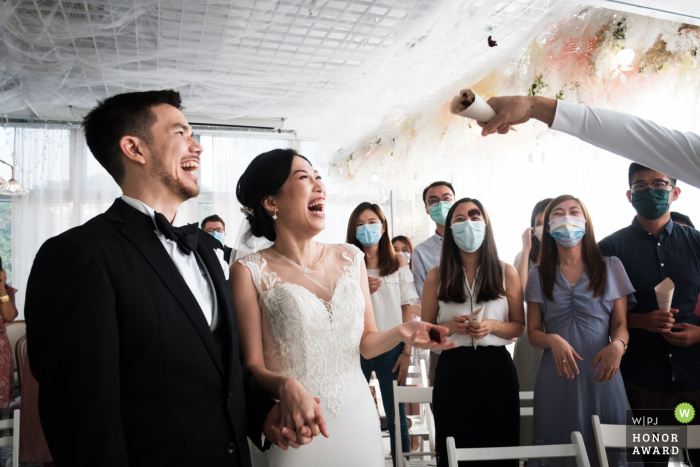 Ein außergewöhnliches Hochzeitsbild in der Sunset Area von einem professionellen Fotografen aus Hongkong, das die euphorische Braut und den Bräutigam während des Konfetti-Spaziergangs zeigt